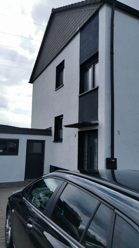 Wohnhaus mit heller Fassade und dunkel abgesetztem Fensterband