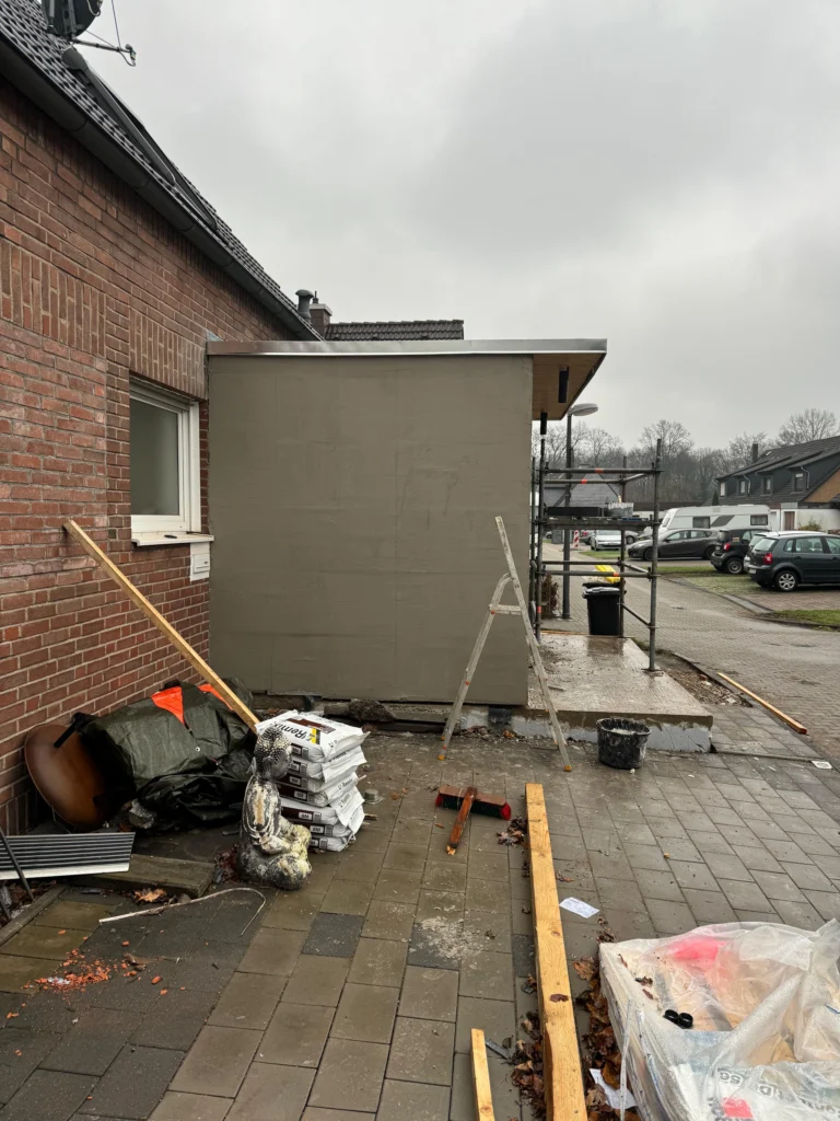Baustelle an einem Anbau mit Baumaterial auf dem Hof