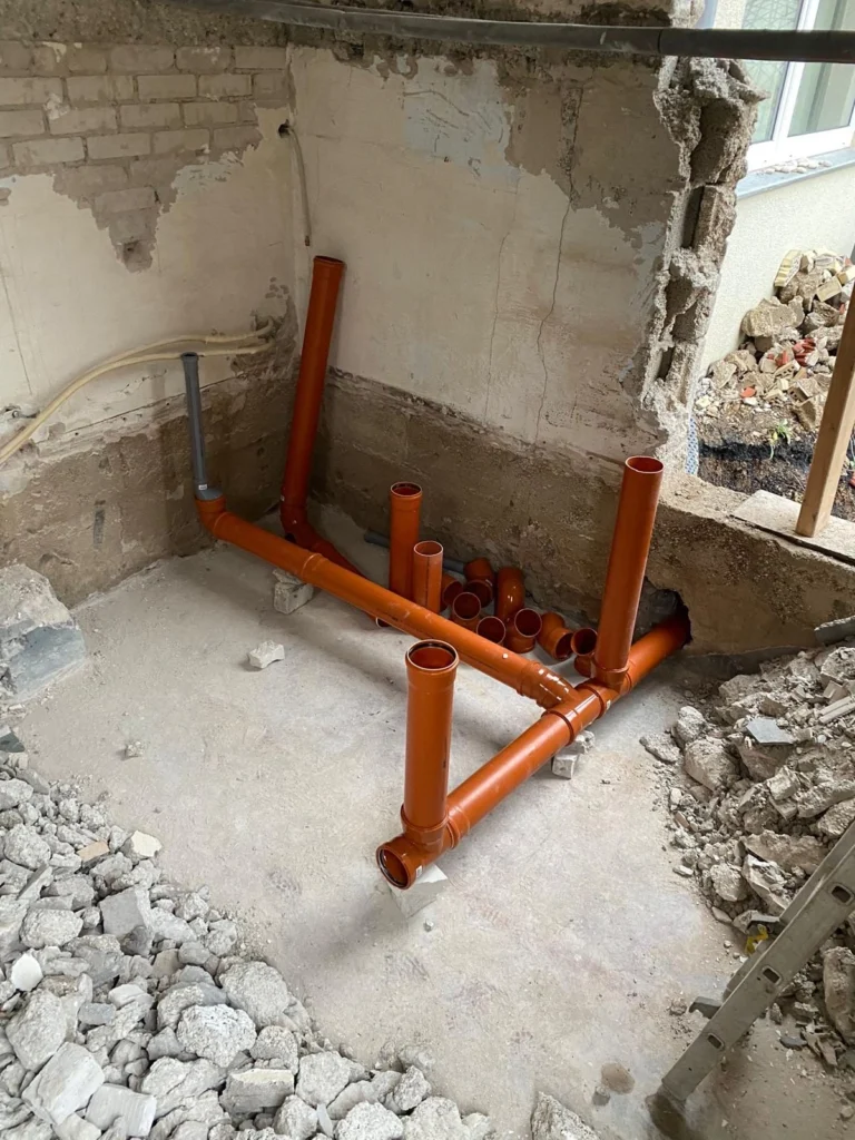 Aufgebrochener Boden mit freigelegten Abwasserrohren und Bauschutt