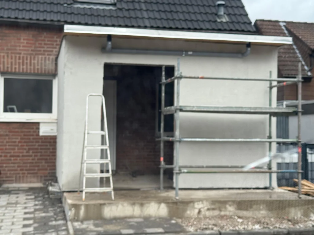 Verputzter Anbau mit Gerüst an einem Backsteinhaus