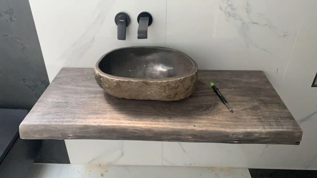 Aufsatzwaschbecken aus Naturstein auf einer Holzplatte vor Marmorfliesen