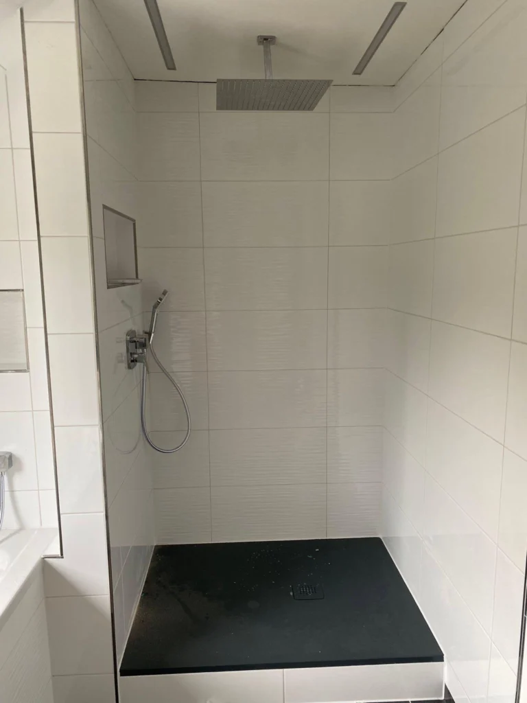 Saubere Dusche mit weißen Wandfliesen und dunkler Duschwanne
