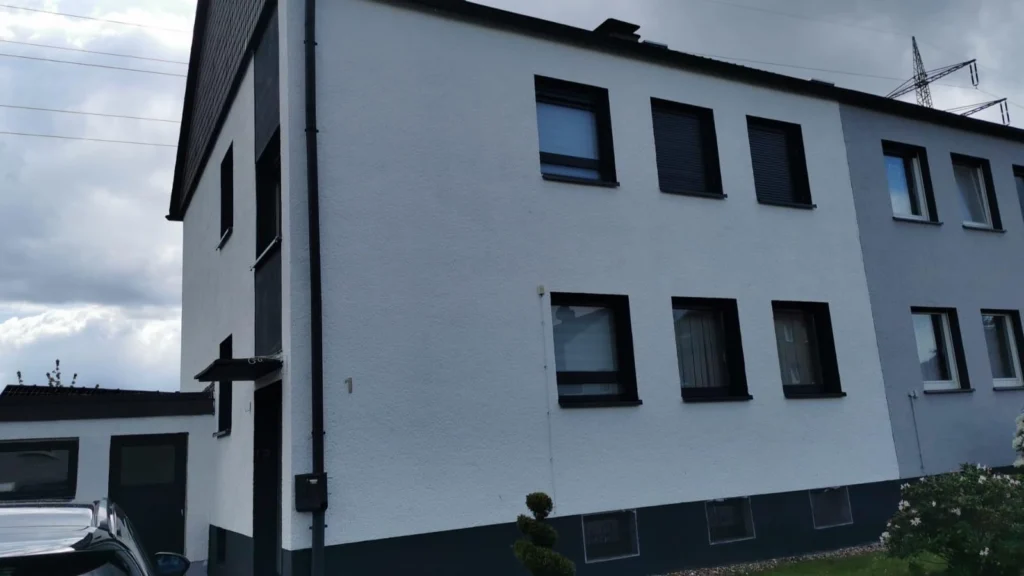 Mehrfamilienhaus mit frisch verputzter weißer Fassade und dunklem Sockel
