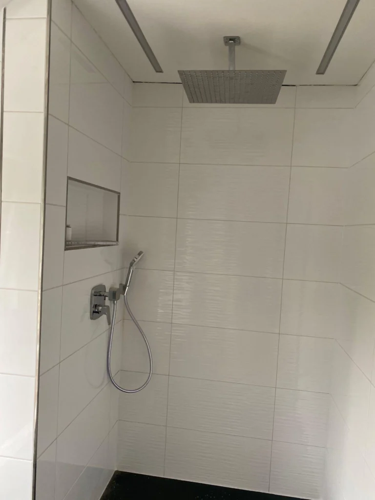 Weiß geflieste bodengleiche Dusche mit Regenbrause und Wandnische