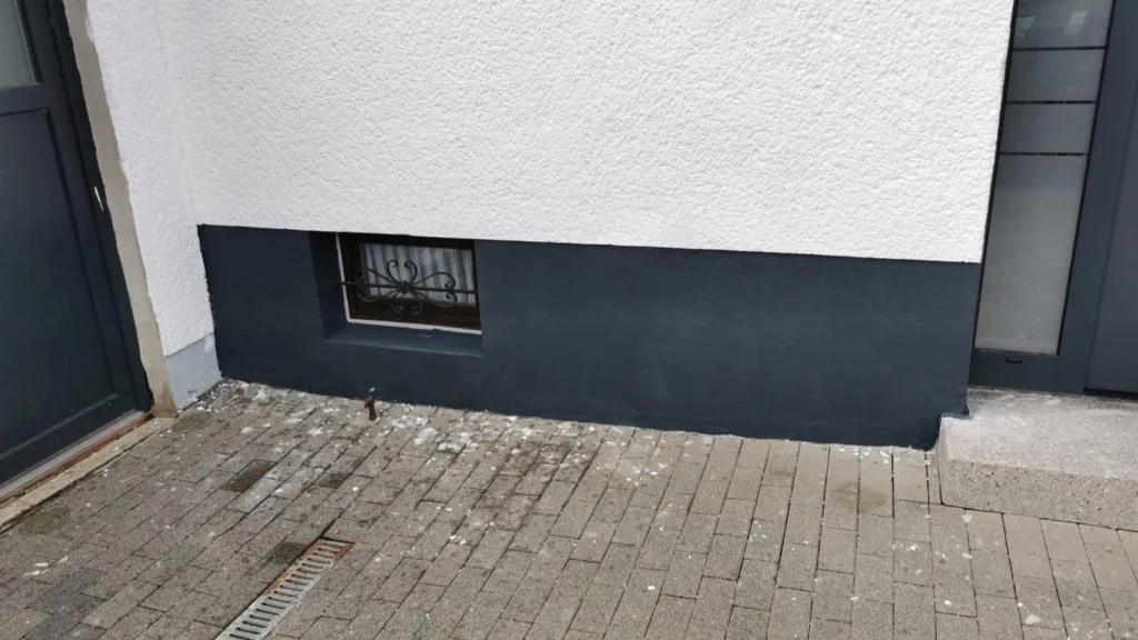 Sockelbereich einer Hauswand mit Kellerfenster und neuer Abdichtung