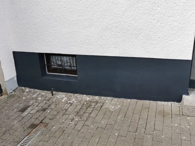 Sockelbereich einer Hauswand mit Kellerfenster und neuer Abdichtung