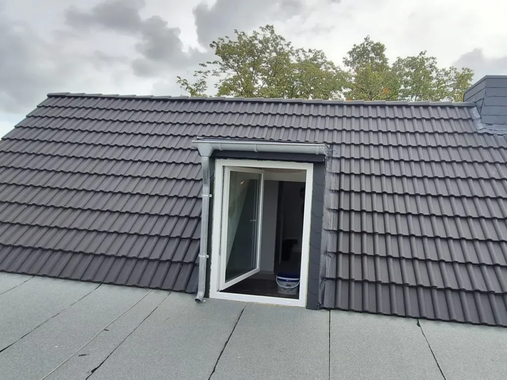 Eingedeckte Dachfläche mit Gaubenfenster, im Vordergrund ein abgedichtetes Flachdach