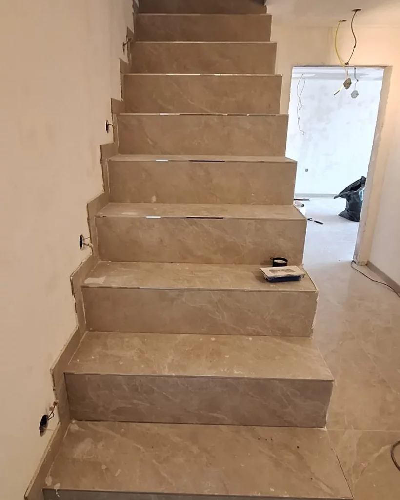 Treppe mit großformatigen Fliesen in Marmoroptik auf Tritt- und Setzstufen, Wände frisch verputzt